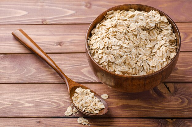 Oat flakes in wooden bowl on wooden rustic background.