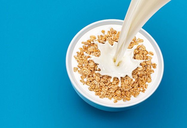 Oat granola with pouring milk and splash isolated on blue background top view