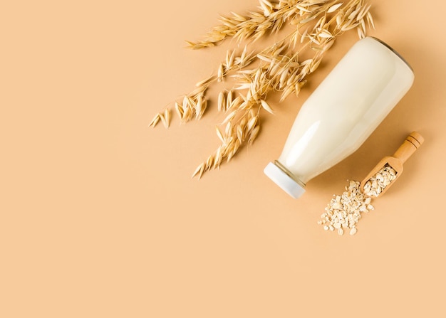 Oat milk in glass bottle with flakes and spike or ears of grain on beige background