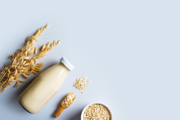 Photo oat milk in glass bottle with flakes and spike or ears of grain on blue background