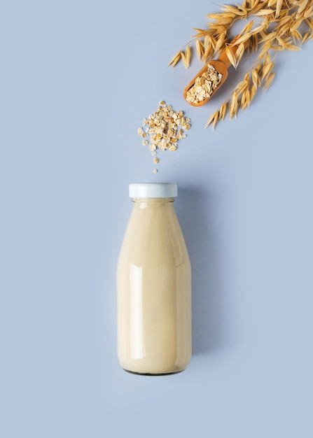 Oat milk in glass bottle with flakes and spike or ears of grain on blue background