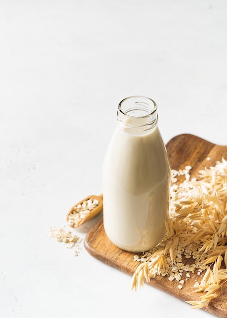 Photo oat milk in glass bottle with flakes and spike or ears of grain on white background