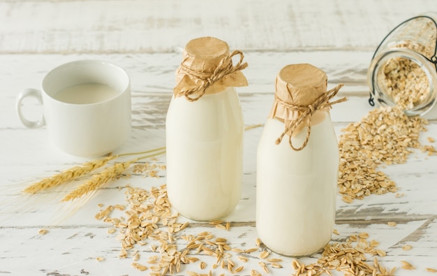 Latte d'avena in bottiglie di vetro e farina d'avena in una tazza su un tavolo di legno.