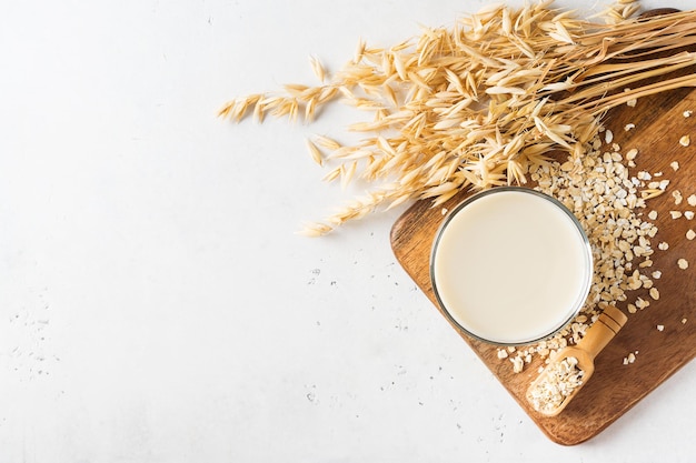 Photo oat milk in glass with flakes and spike or ears of grain on white background