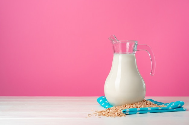 Oat milk in glassware and dry oat flakes on pink background close up