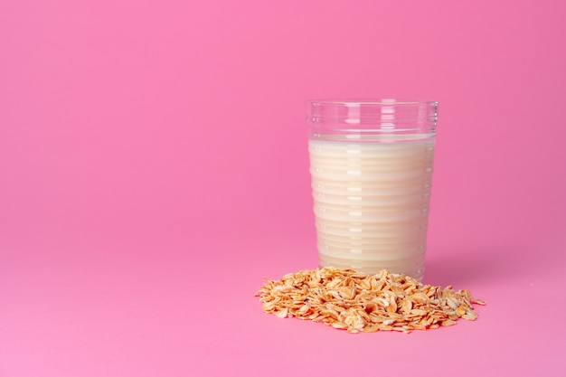 Oat milk in glassware and dry oat flakes on pink  close up