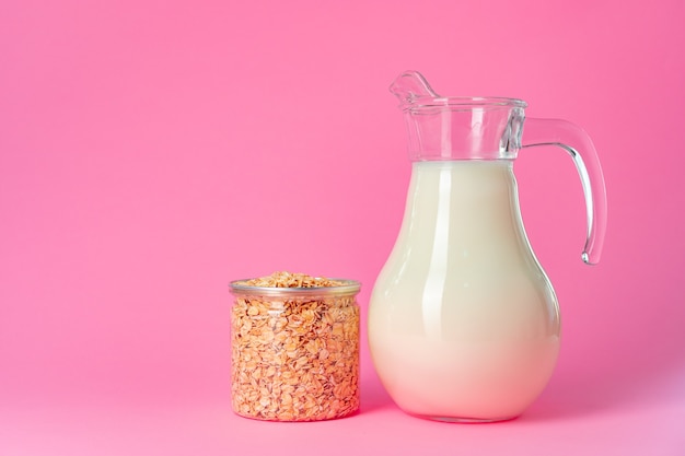 Oat milk in glassware and dry oat flakes on pink