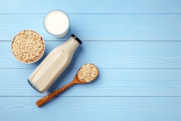 Oat milk and oat flakes in bowl on blue table