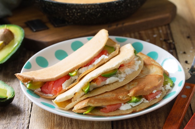 Oat pancakes stuffed with cottage cheese salmon and avocado in a plate on rustic wooden table