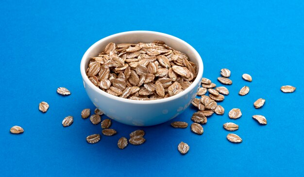 Oat rye flakes in bowl isolated on blue color 