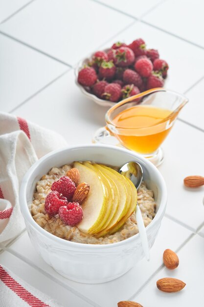 Oatmeal Bowl of oatmeal porridge with raspberry pear and honey on gray concrete old table background Hot and healthy food for Breakfast top view flat lay