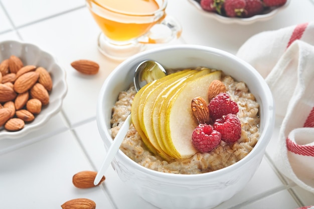 Oatmeal Bowl of oatmeal porridge with raspberry pear and honey on gray concrete old table background Hot and healthy food for Breakfast top view flat lay