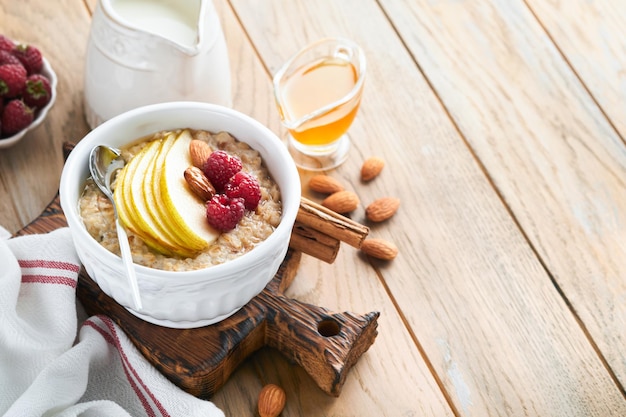 Ciotola di farina d'avena di porridge di farina d'avena con pera lampone e miele su sfondo di tavolo in legno vecchio cibo caldo e sano per colazione vista dall'alto laici piatta