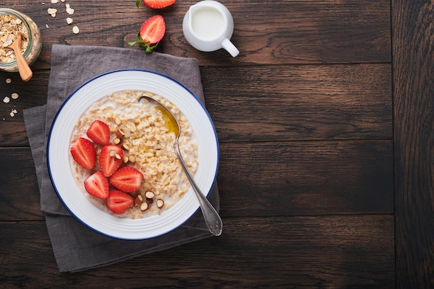 Oatmeal Bowl of oatmeal porridge with strawberry almond and milk on old wooden dark table background Top view in flat lay style Natural ingredients Hot and healthy breakfast and diet food