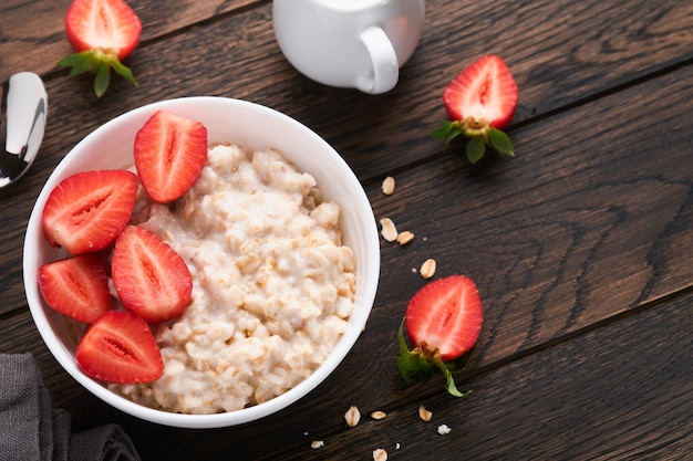 Oatmeal Bowl of oatmeal porridge with strawberry almond and milk on old wooden dark table background Top view in flat lay style Natural ingredients Hot and healthy breakfast and diet food