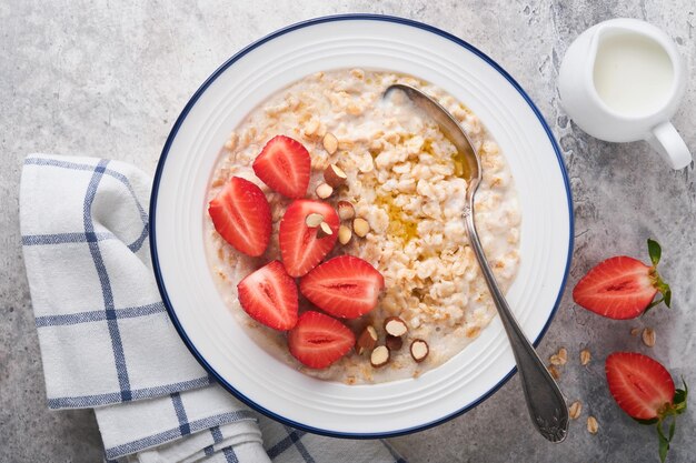 Oatmeal Bowl of oatmeal porridge with strawberry almond and milk on old wooden dark table background Top view in flat lay style Natural ingredients Hot and healthy breakfast and diet food