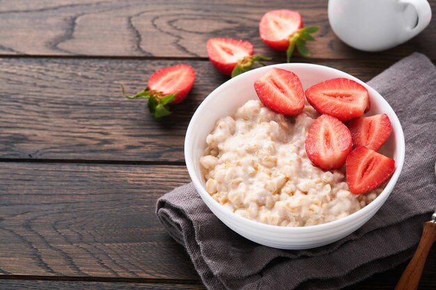 Oatmeal bowl of oatmeal porridge with strawberry almond and
milk on old wooden dark table background top view in flat lay style
natural ingredients hot and healthy breakfast and diet food