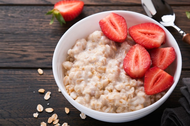 Oatmeal bowl of oatmeal porridge with strawberry almond and\
milk on old wooden dark table background top view in flat lay style\
natural ingredients hot and healthy breakfast and diet food