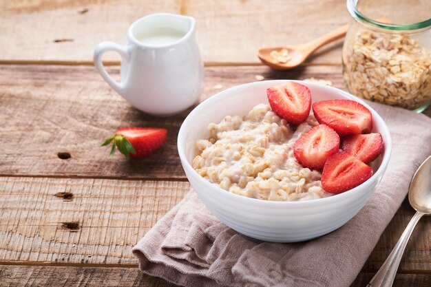 Oatmeal Bowl of oatmeal porridge with strawberry almond and milk on old wooden dark table background Top view in flat lay style Natural ingredients Hot and healthy breakfast and diet food