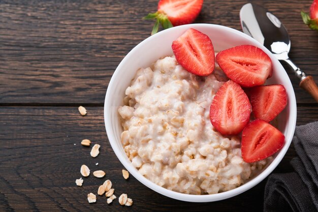 Oatmeal Bowl of oatmeal porridge with strawberry almond and milk on old wooden dark table background Top view in flat lay style Natural ingredients Hot and healthy breakfast and diet food