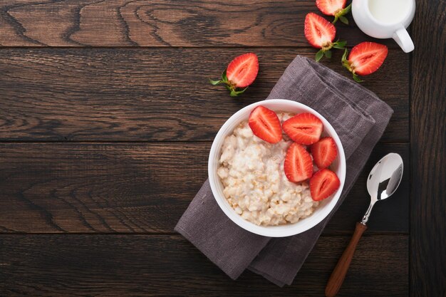 Oatmeal Bowl of oatmeal porridge with strawberry almond and milk on old wooden dark table background Top view in flat lay style Natural ingredients Hot and healthy breakfast and diet food