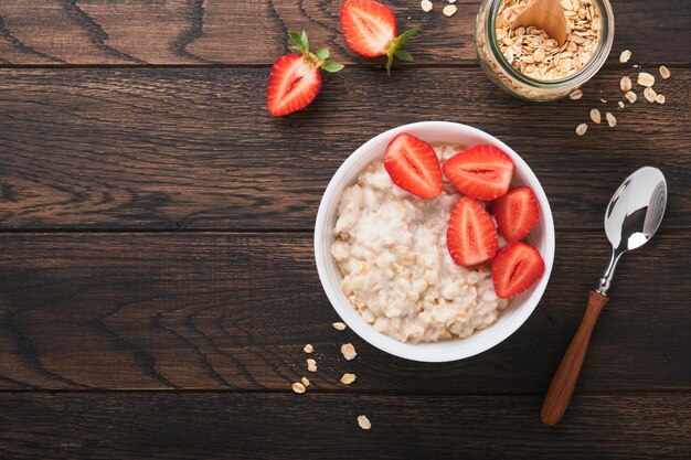 Ciotola di farina d'avena con porridge di farina d'avena con fragola, mandorla e latte su vecchio sfondo di tavolo in legno scuro vista dall'alto in stile piatto ingredienti naturali colazione calda e sana e cibo dietetico