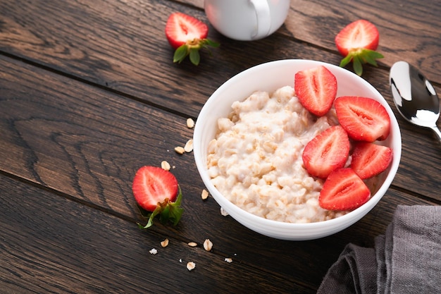 Oatmeal Bowl of oatmeal porridge with strawberry almond and milk on old wooden dark table background Top view in flat lay style Natural ingredients Hot and healthy breakfast and diet food