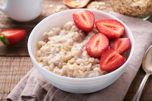 Oatmeal Bowl of oatmeal porridge with strawberry almond and milk on old wooden dark table background Top view in flat lay style Natural ingredients Hot and healthy breakfast and diet food