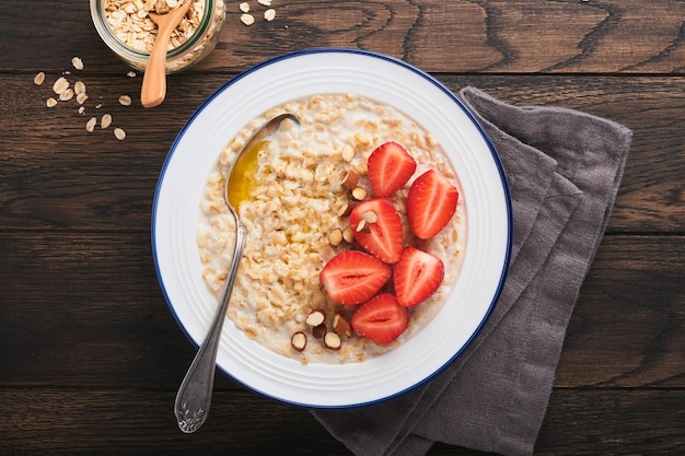 Ciotola di farina d'avena con porridge di farina d'avena con fragola, mandorla e latte su vecchio sfondo di tavolo in legno scuro vista dall'alto in stile piatto ingredienti naturali colazione calda e sana e cibo dietetico