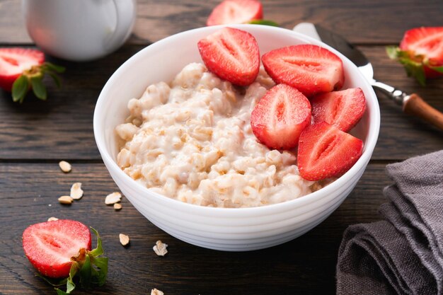 Ciotola di farina d'avena con porridge di farina d'avena con fragola, mandorla e latte su vecchio sfondo di tavolo in legno scuro vista dall'alto in stile piatto ingredienti naturali colazione calda e sana e cibo dietetico