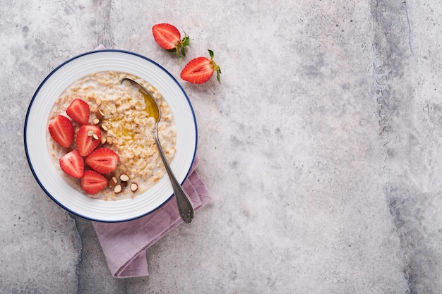 Oatmeal Bowl of oatmeal porridge with strawberry almond and milk on vintage light grey teal table Top view in flat lay style Natural ingredients Hot and healthy breakfast and diet food