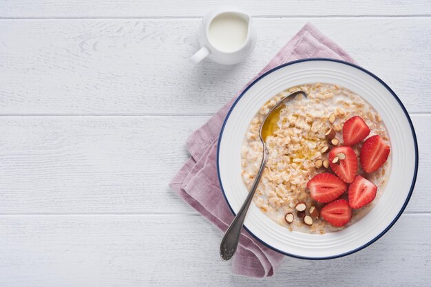 白い​木製​の​テーブル​の​背景​に​ストロベリー​アーモンド​と​ミルク​と​オートミール​の​お​粥​の​オートミールボウルフラットレイスタイル​の​上面図​天然​成分​温かくて​健康的​な​朝食​の​朝​と​ダイエット​食品