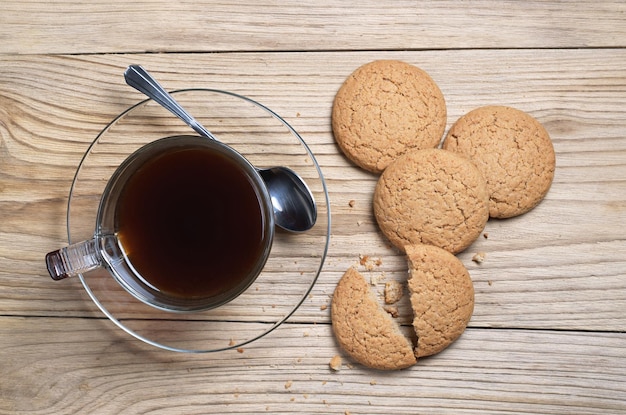 Photo oatmeal cookies and black coffee in a transparent cup for breakfast on old wooden background top view