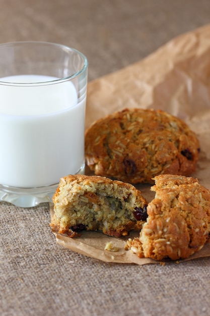 Oatmeal cookies broken and a glass of milk on paper wrapping kraft and on burlap tablecloth.