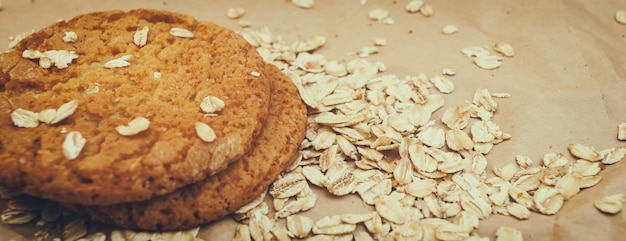 Photo oatmeal cookies and oat flakes scattered on panaramnom background crumpled paper