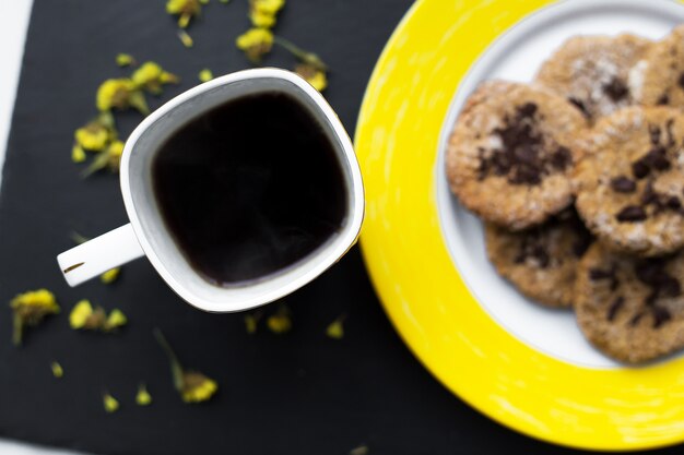 Овсяное печенье с шоколадом на ярко-желтой тарелке и чашке кофе