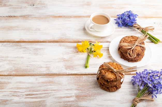 oatmeal cookies with snowdrop flowers bluebells, narcissus and cup of coffee on white background.