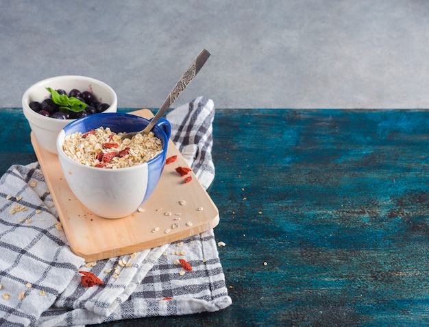 Oatmeal in cup with berries in bowl on wooden board