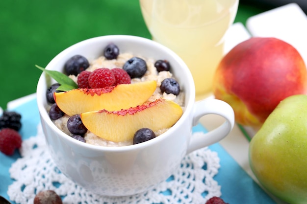 Oatmeal in cup with berries on napkin on table on grass background