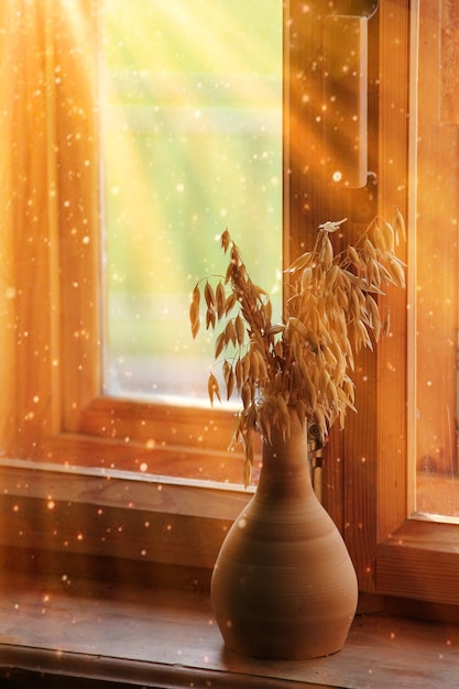 写真 太陽の下で木製の窓を背景に、粘土の花瓶のオートミールの耳