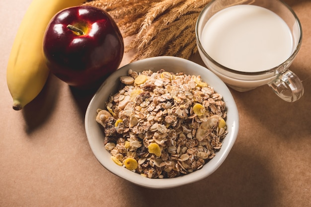 Oatmeal flakes in a bowl, milk, apple and banana on wooden table. 