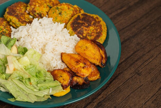 Oatmeal fritters vegetables fried ripe bananas and white rice served on a plate on a wooden table