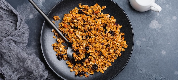 Oatmeal granola with yoghurt, fresh strawberries and banana, chia seeds, sunflower and honey in black ceramic plate on dark background. Top view