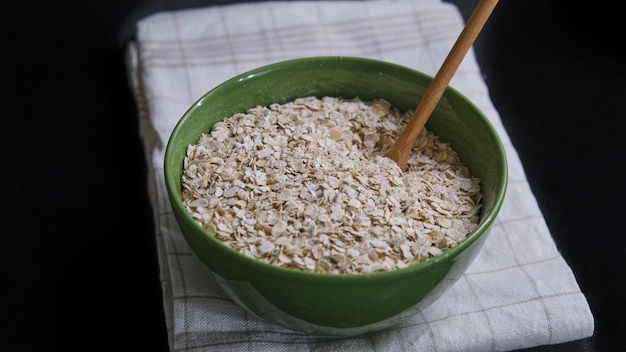 Oatmeal in a green bowl on a brown and white cloth in the kitchen on a black background. Dark food