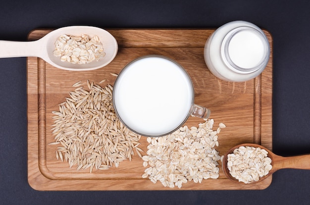 Oatmeal milk with oat seeds on wooden background