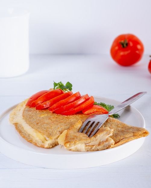Oatmeal pancake with melted cheese and red tomato on white wooden table