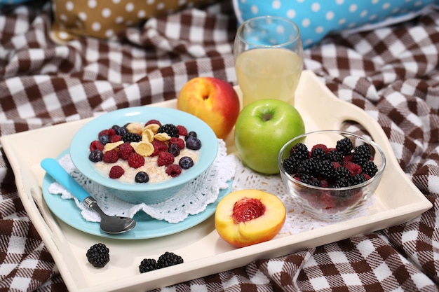 Oatmeal in plate with berries on napkins on wooden tray on bad