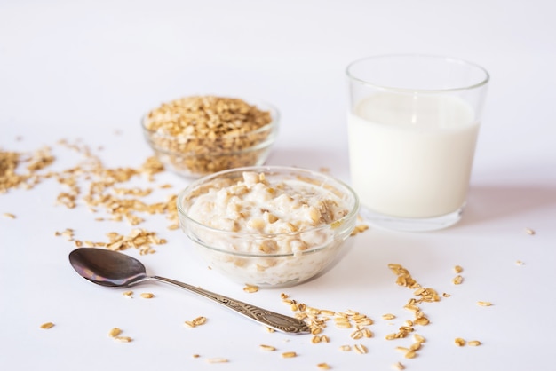 Oatmeal in a plate with a glass of milk and a spoon on a white surface.