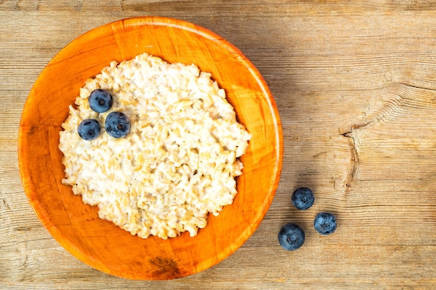 Oatmeal porridge and blueberry in orange bamboo bowl on wooden table background