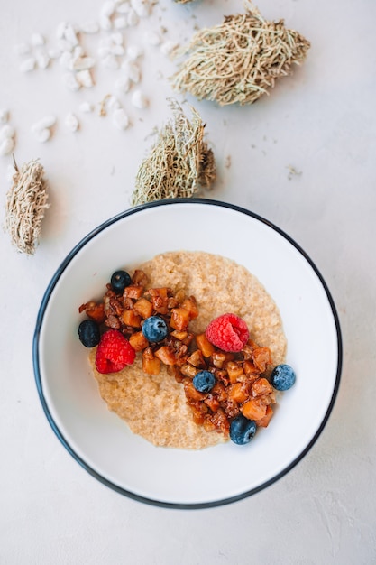 Oatmeal porridge in bowl topped with fresh blueberries, cranberries and homemade crunchy granola